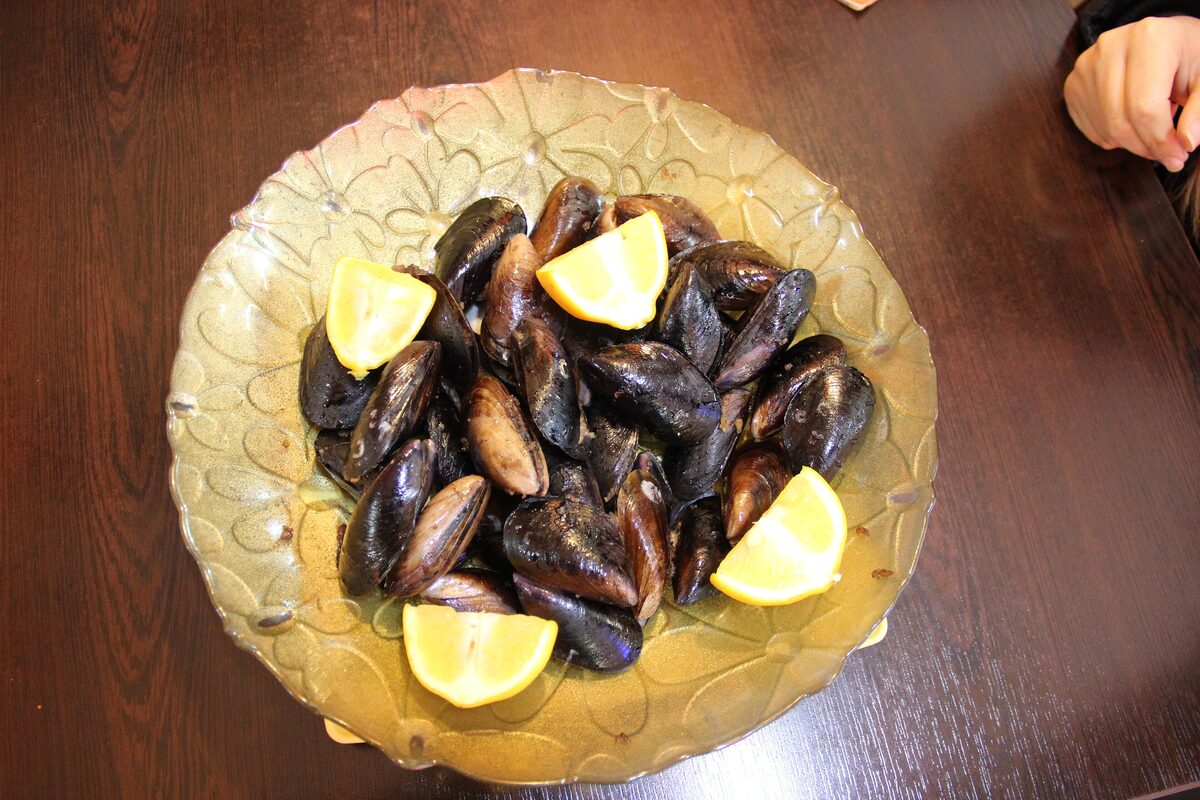 A glass plate of black stuffed mussels with lemon wedges
