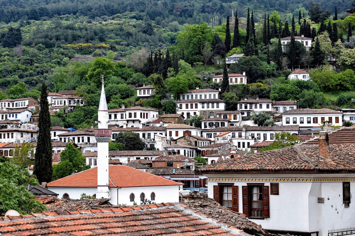 The white houses and red roofs of Şirince climbing a green hillside, with a slender minaret in the middle and cypress trees above
