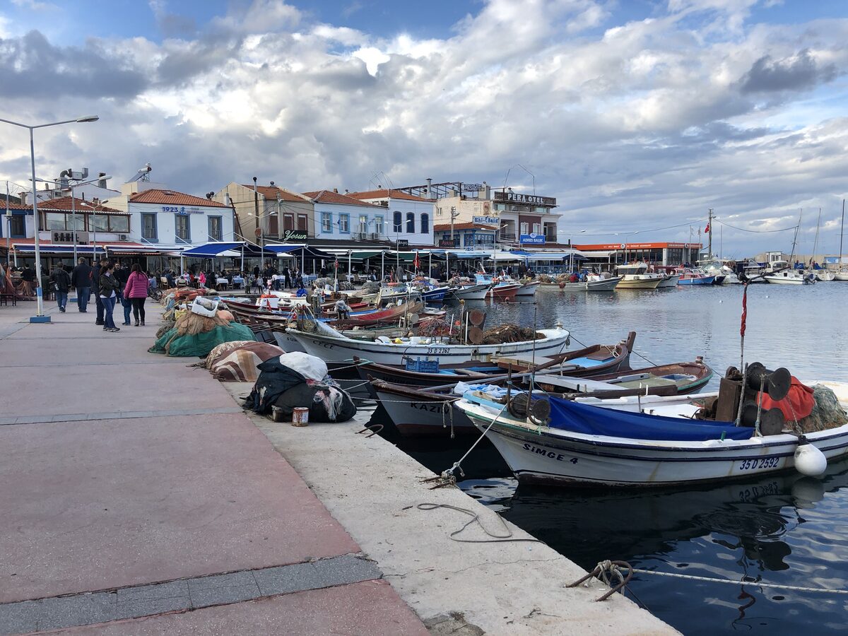 Fishing boats tied up along the harbor of Urla İskele, with low waterfront restaurants and cafés behind them