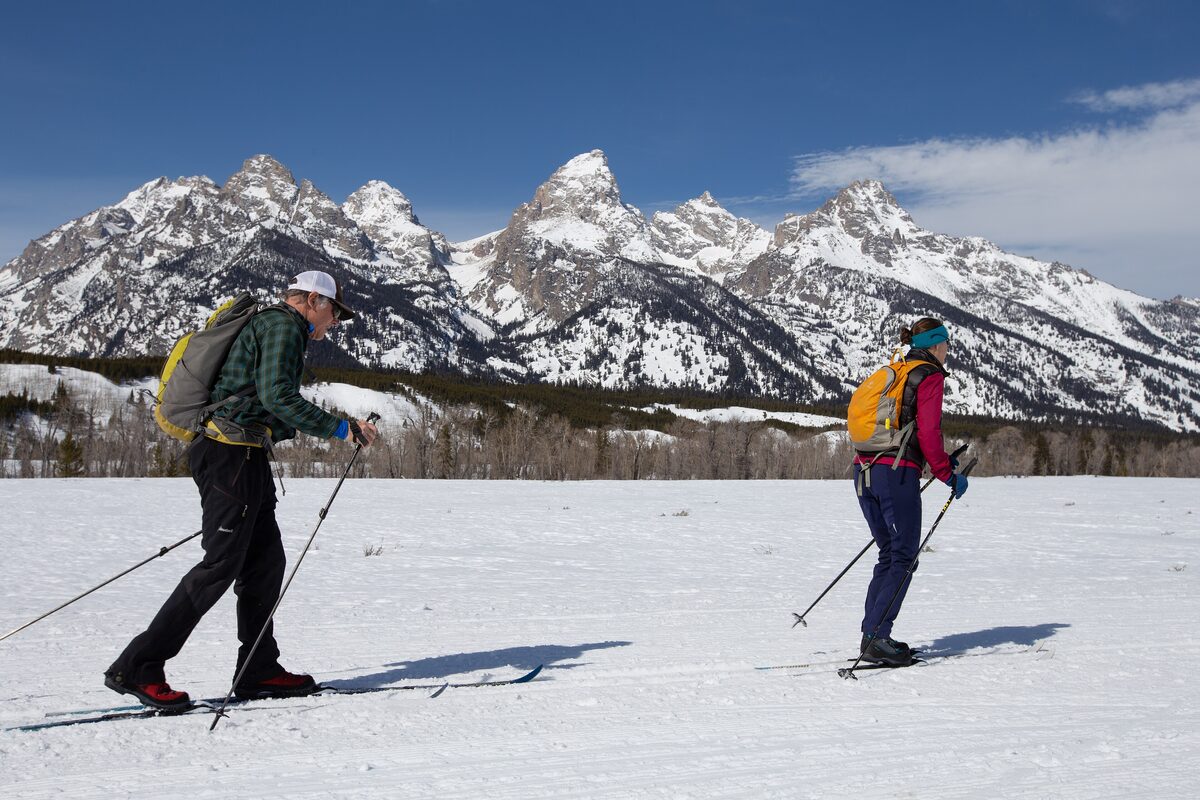 Two cross-country skiers on snow with the jagged Teton peaks behind them