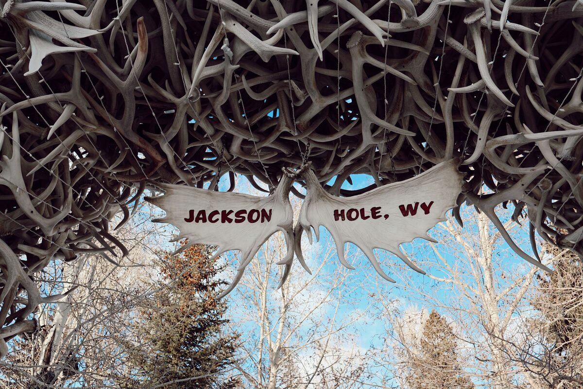 Looking up under an elk antler arch on the Jackson Town Square, with the Jackson Hole, WY sign and bare trees against a blue sky
