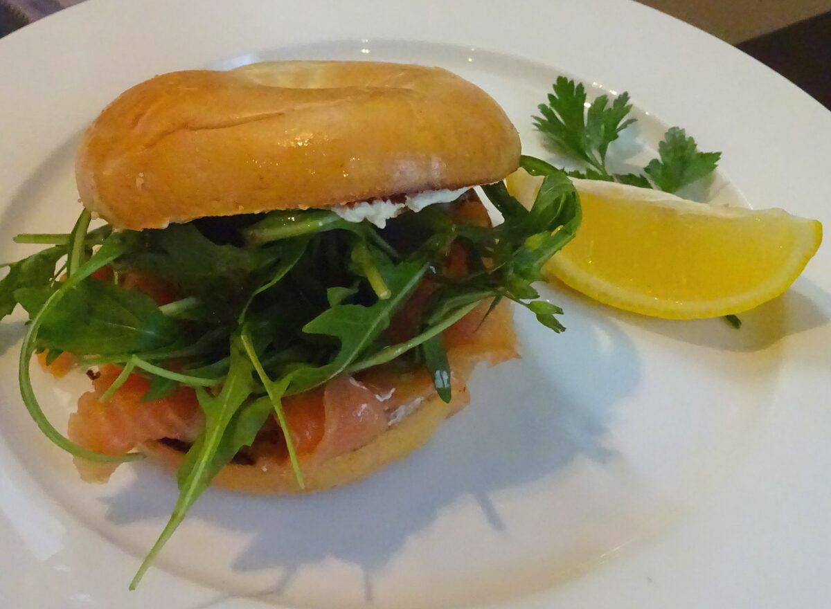 A bagel sandwich with smoked salmon, arugula and cream cheese on a plate with a lemon wedge