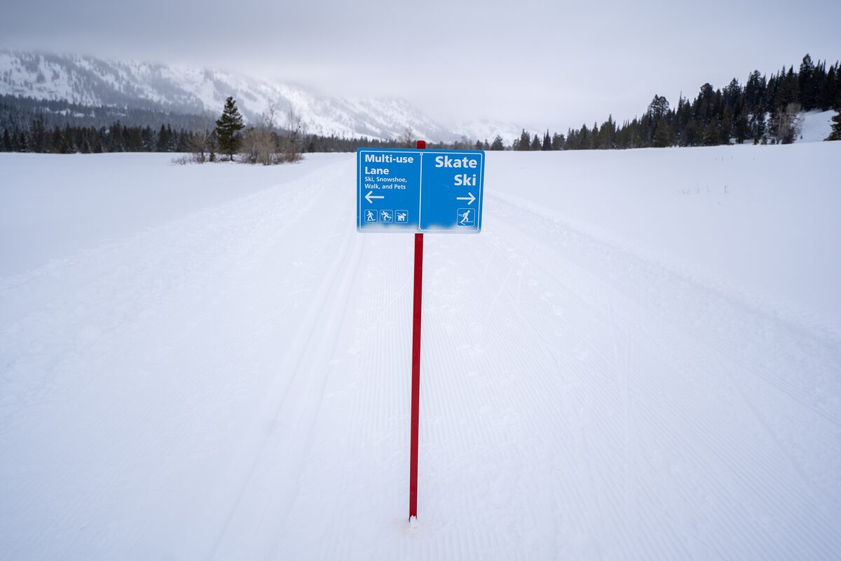 A groomed winter trail beside a blue Multi-use Lake and Skate Ski sign on the snowy Teton Park Road