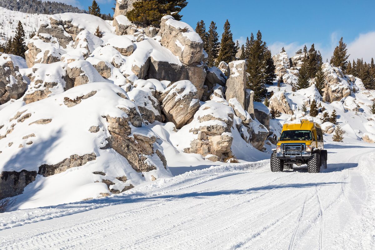 A yellow snowcoach on a snow-packed road between snow-covered rock formations in Yellowstone