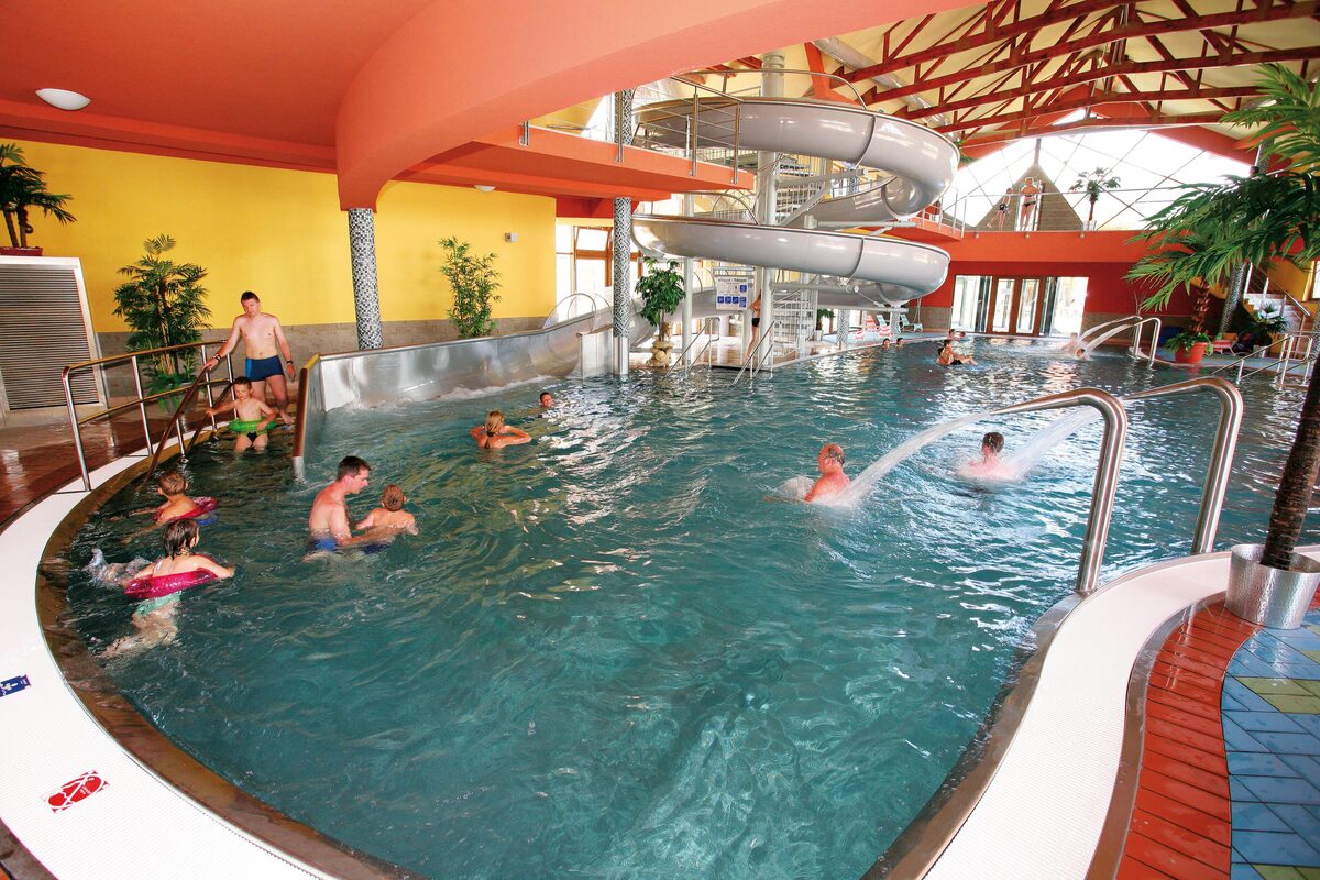 An indoor thermal pool with a spiral water slide under a timber roof at Bešeňová
