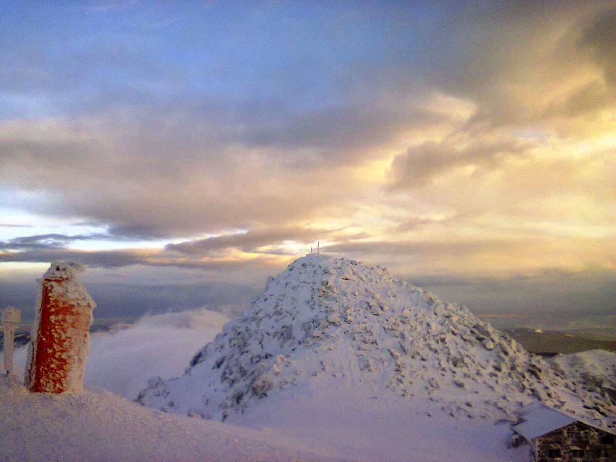 The snow-covered Chopok summit cone under a golden evening sky, with a frost-coated red post at the left edge