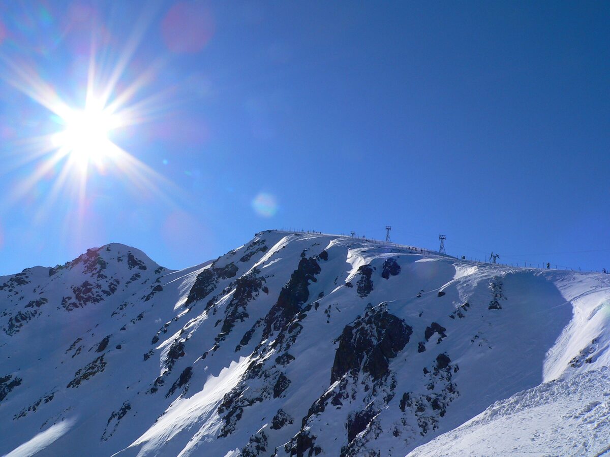 Chopok's snowy ridge under a blue sky with the sun flaring over the summit