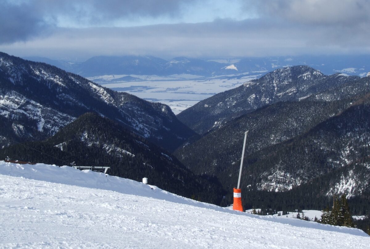 A snowy valley seen from a Jasná slope, with forested hillsides and distant mountains