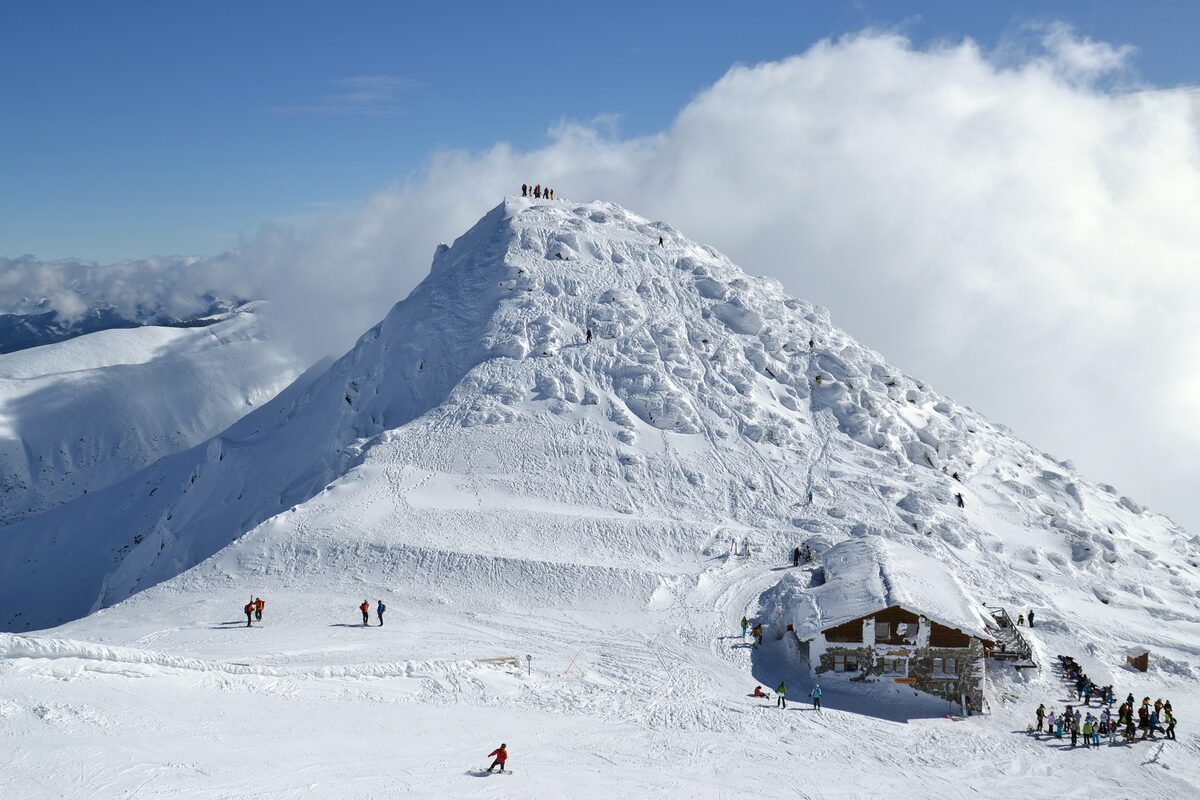 A mountain hut below a steep snow-covered slope on Chopok, with skiers in front