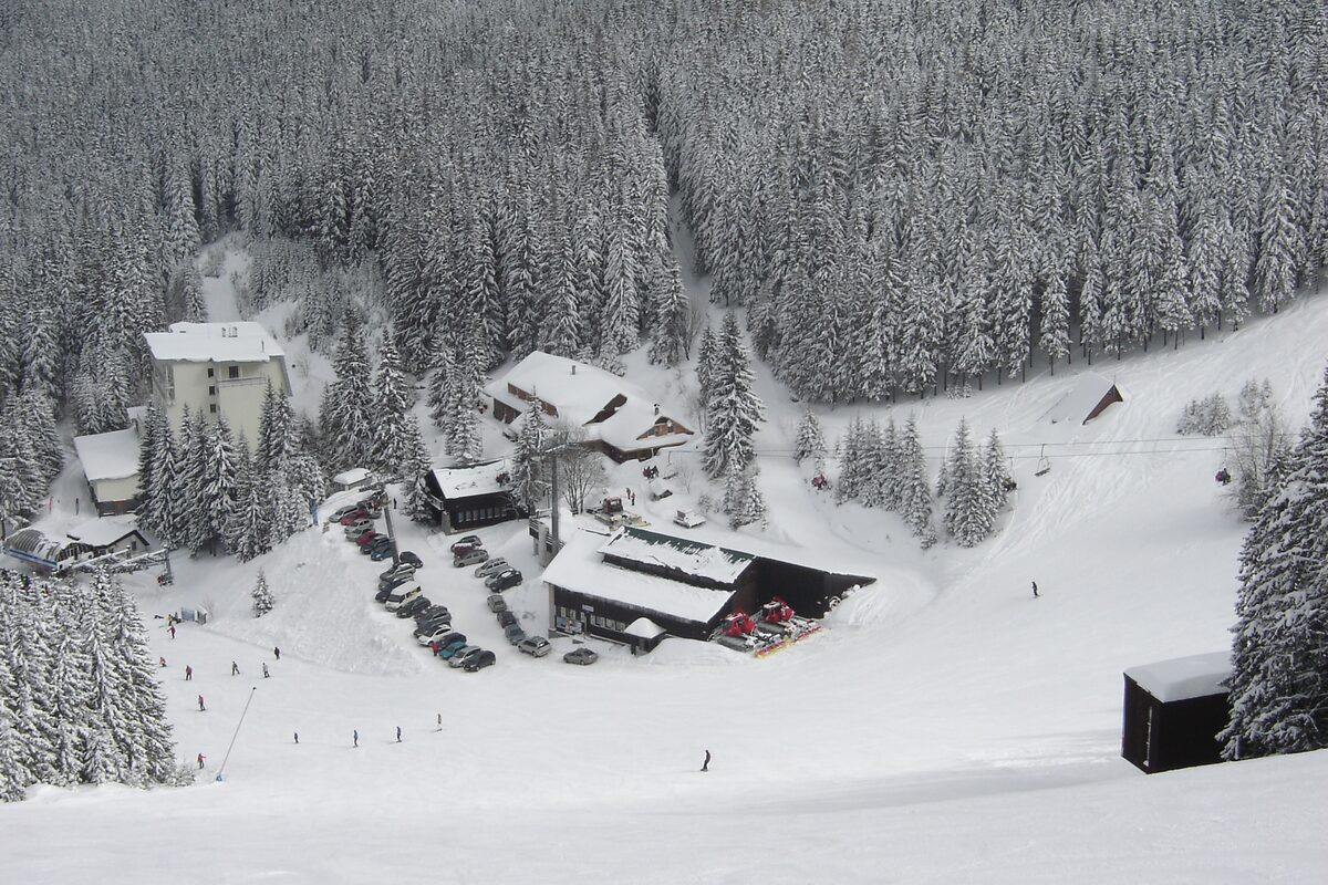 Lodges and chalets in deep snow beside the Koliesko valley station, with spruce forest above