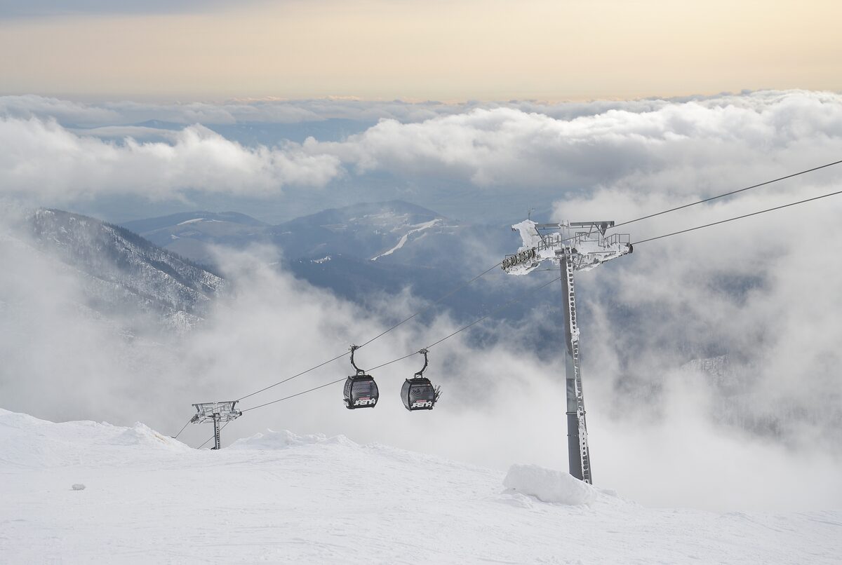 Two gondola cabins hanging from the cable above a valley filled with cloud, with a lift pylon on a snowy slope