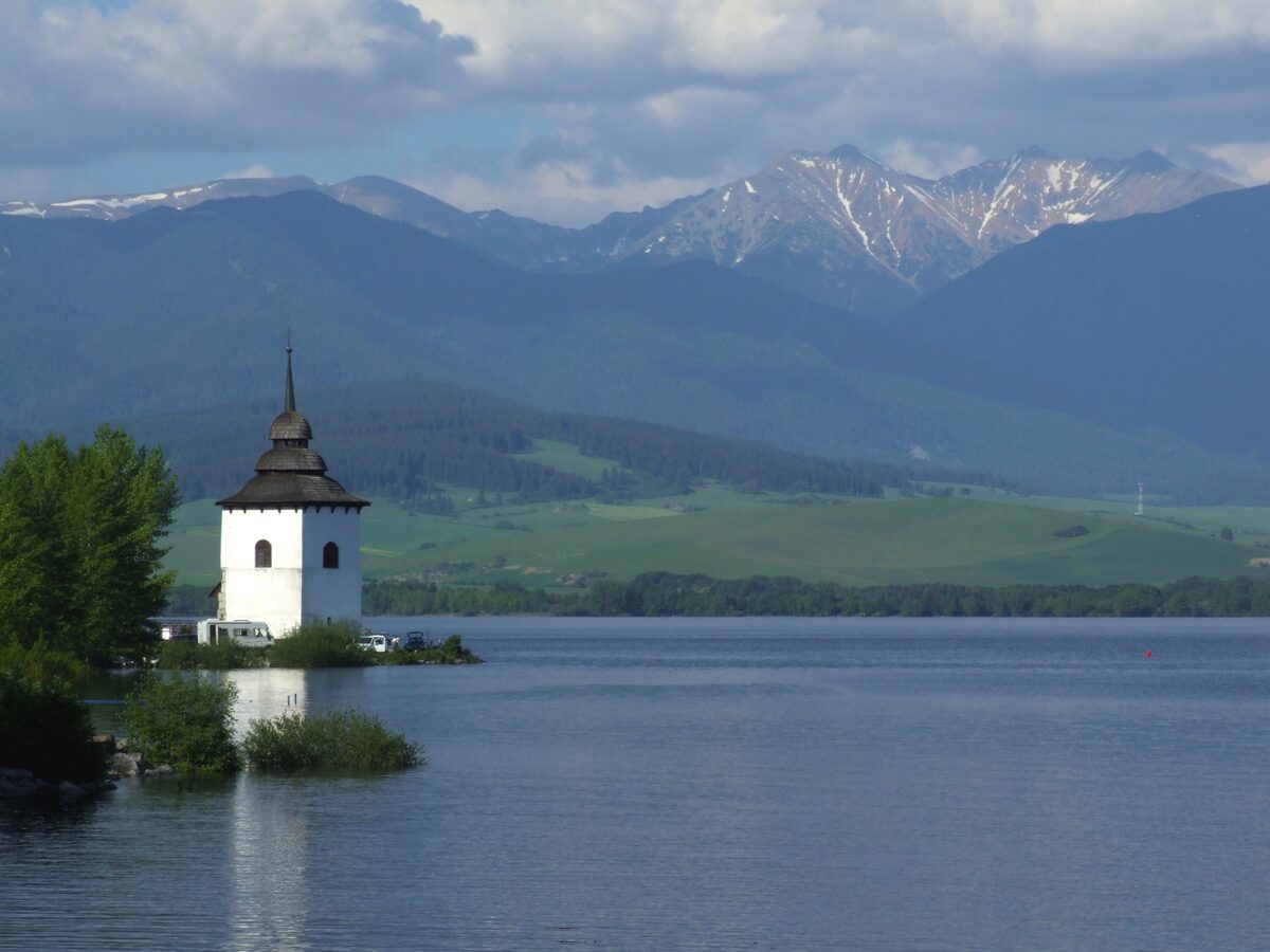 A small white church tower on the water of the Liptovská Mara reservoir, with the Tatra peaks behind