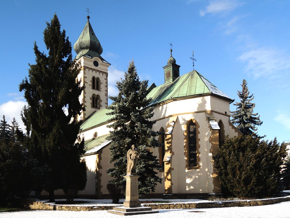 The Church of St. Nicholas in Liptovský Mikuláš, with a green copper tower and a statue on a square with a little snow