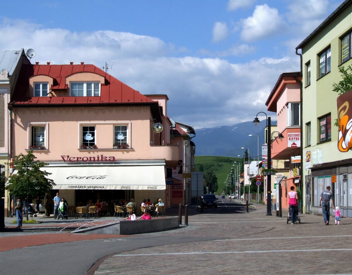 A cobbled town street in Liptovský Mikuláš with a café terrace, shops and green mountains at the end of the street