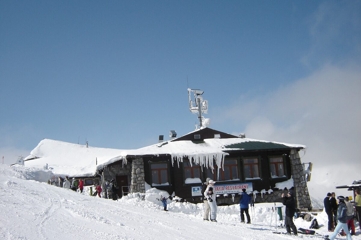 The Luková middle-station building in deep snow, with icicles on the roof and skiers outside