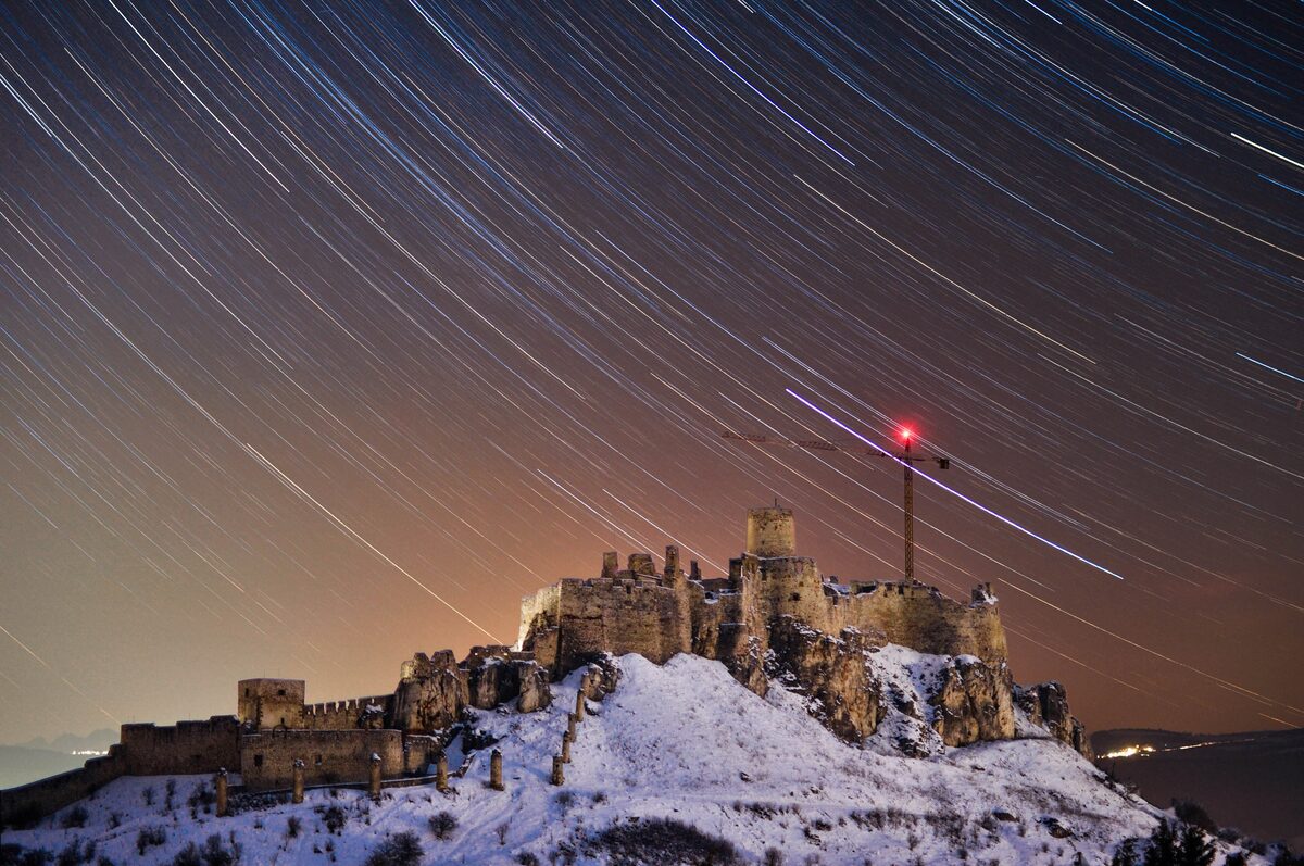 The ruined Spiš Castle on its snow-dusted hill at night, under a sky of star trails
