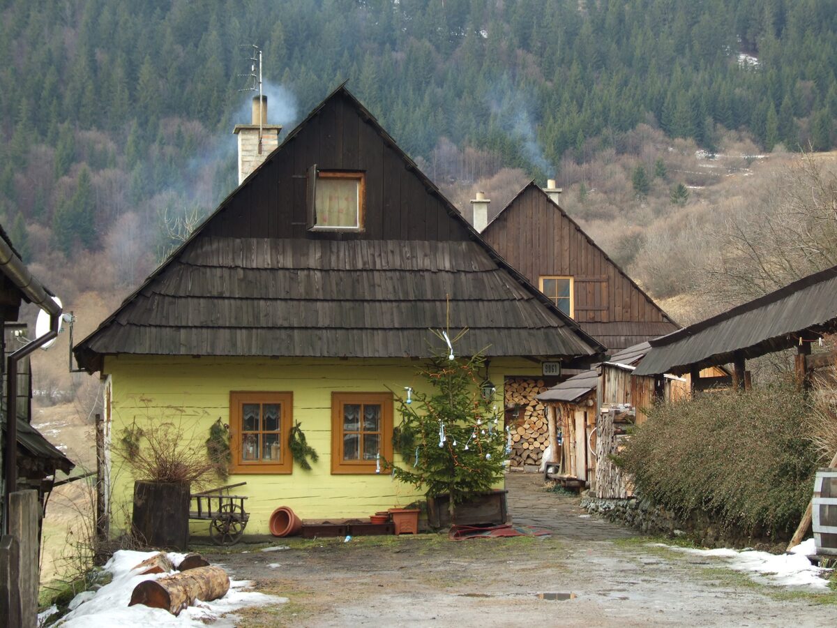 A yellow log house with a shingle roof and snow patches in the village of Vlkolínec