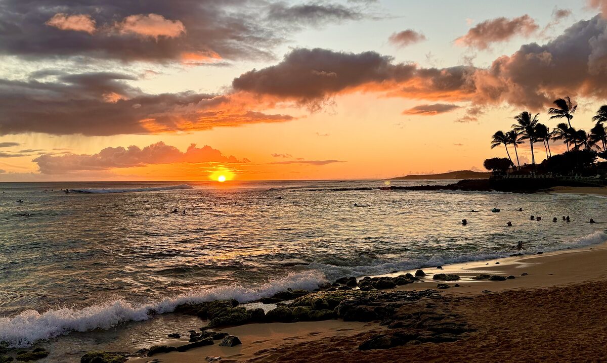 Sun setting behind palms and lava rocks at Poʻipū