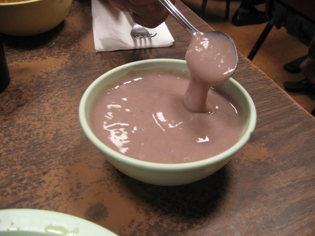 A bowl of purple-grey poi with a spoon lifting some