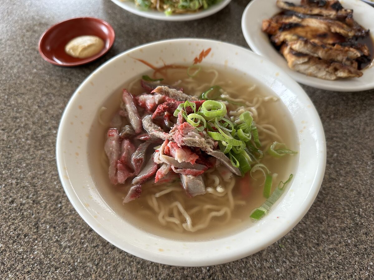 A bowl of saimin noodle soup with sliced pork and green onion