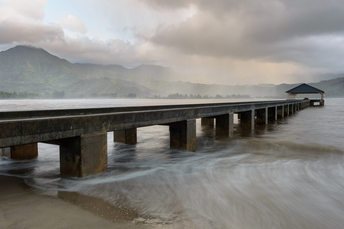 Long Hanalei Pier reaching into the bay beneath green mountains