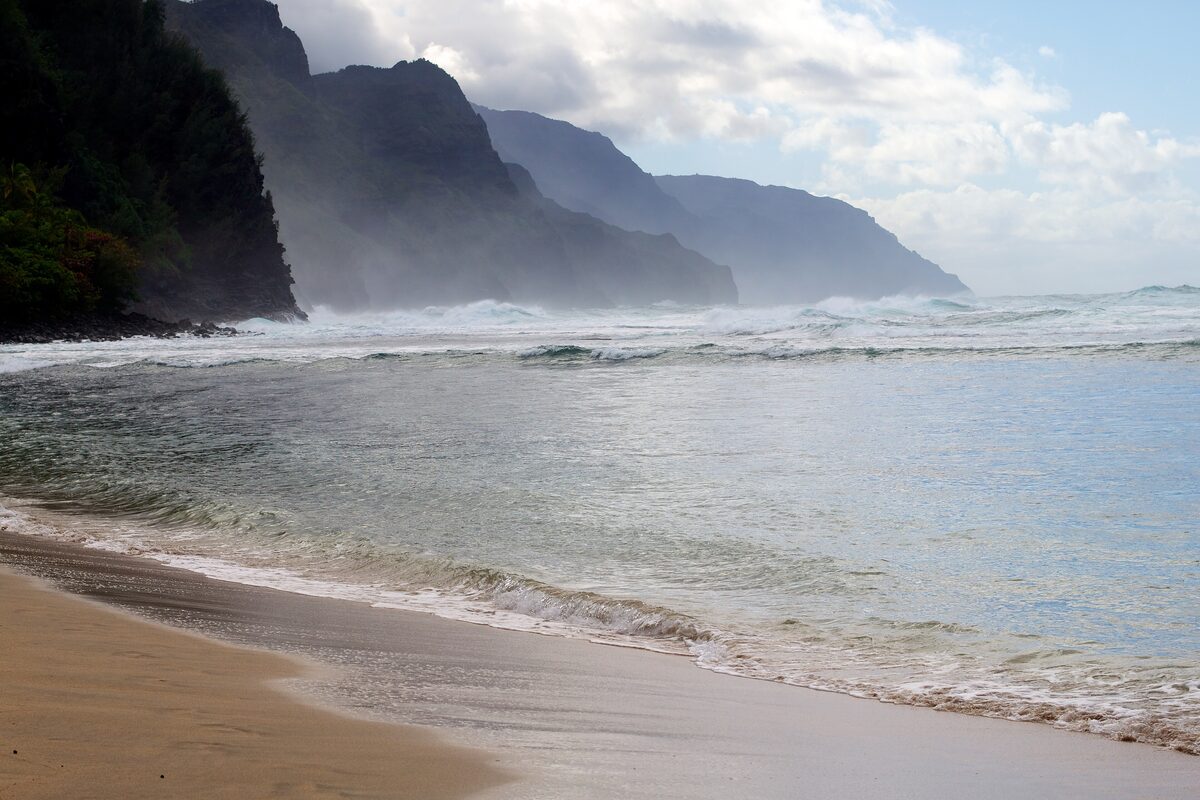 Misty Nā Pali cliffs above the sand of Keʻe Beach
