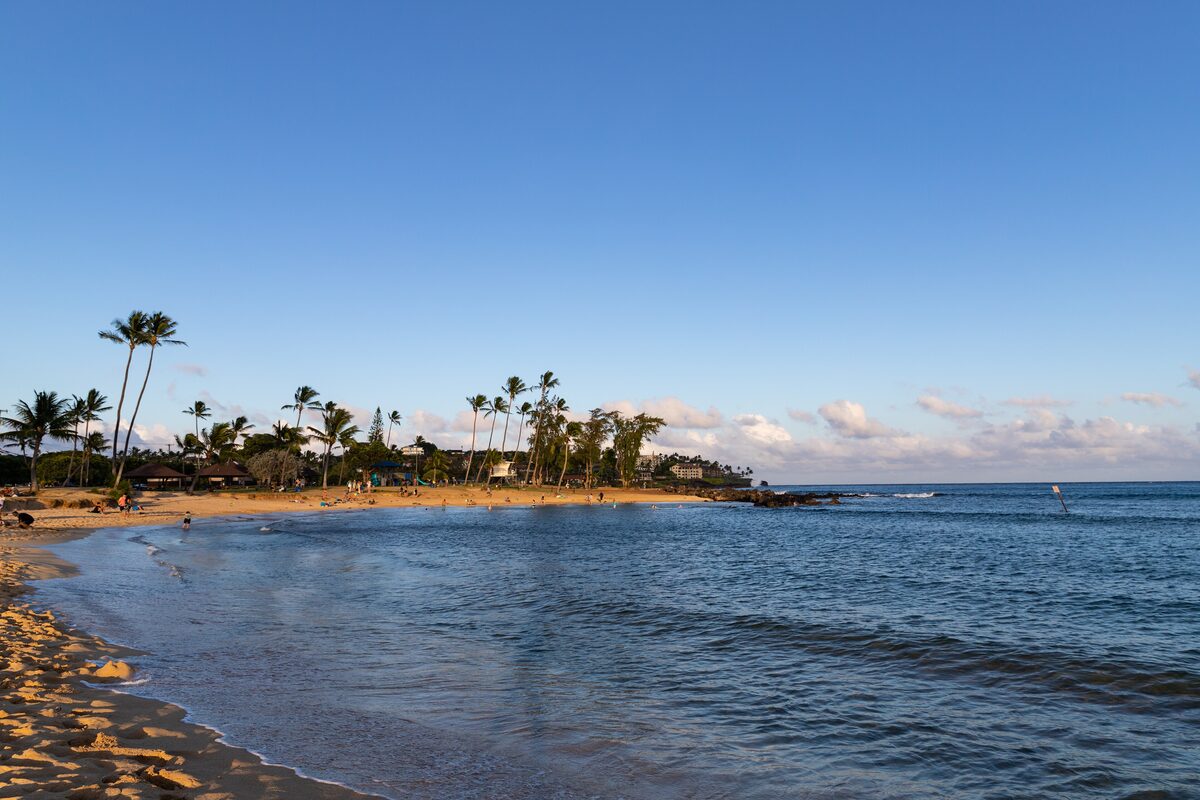 Calm golden crescent of Poʻipū Beach Park lined with palms