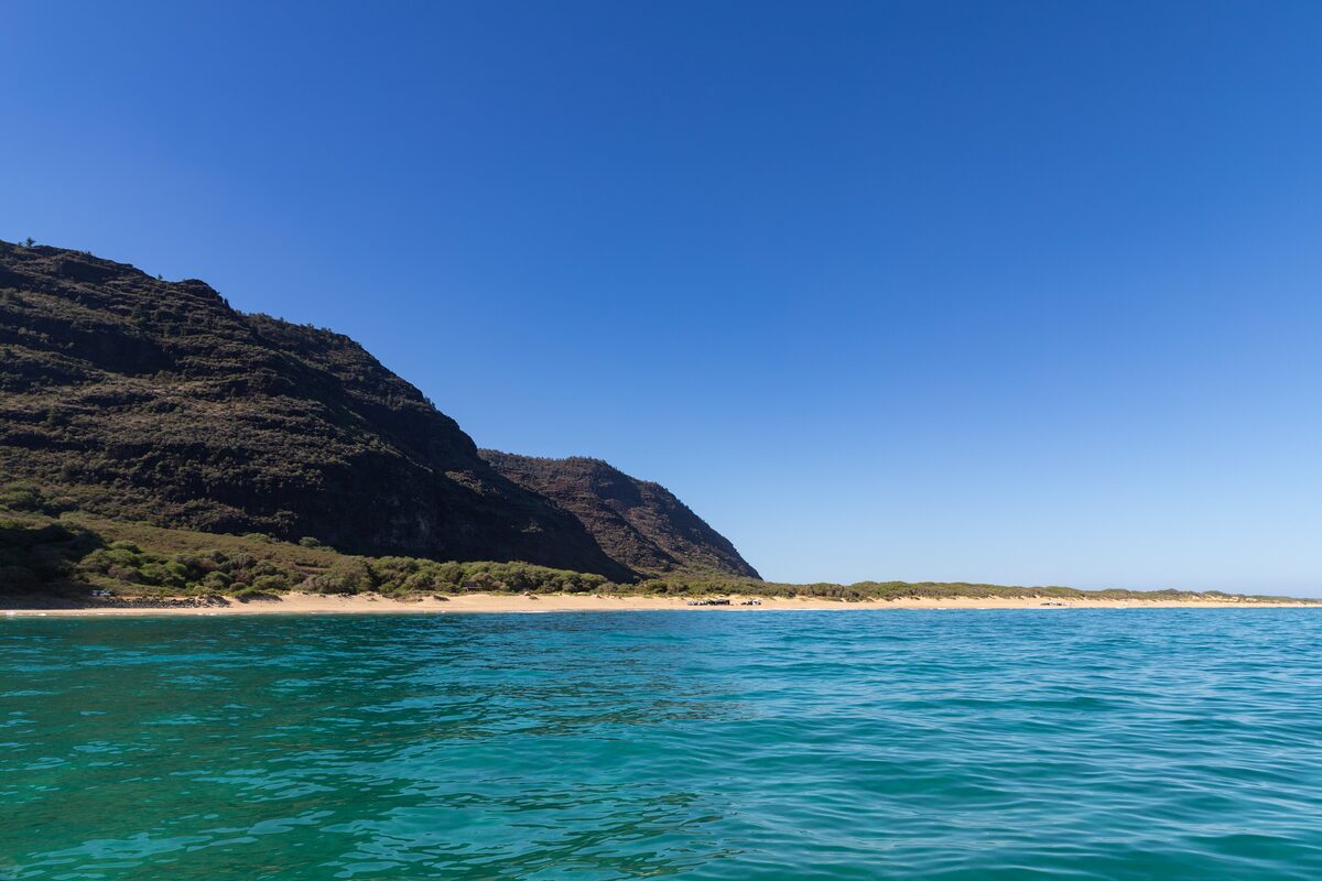 Long pale Polihale beach beneath dark dry cliffs