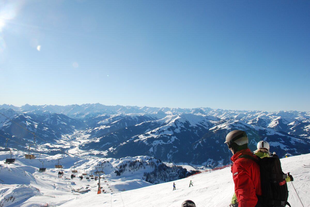 Skiers on a sunny slope of the Kitzbüheler Horn with lifts and a wide snowy valley below