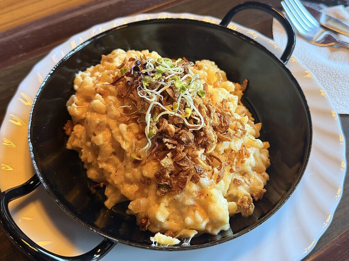 Cheese spätzle in a black pan, topped with crispy fried onions and sprouts