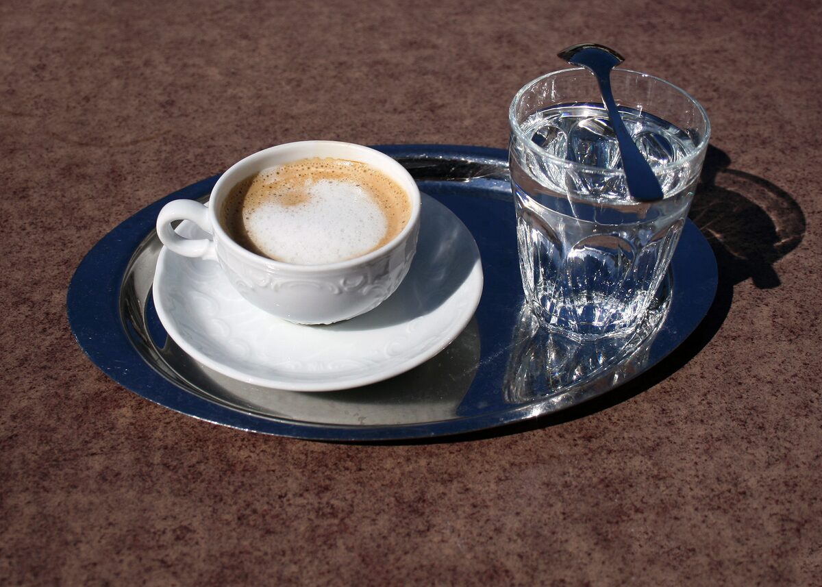A Wiener Melange in a white cup on a silver tray with a glass of water