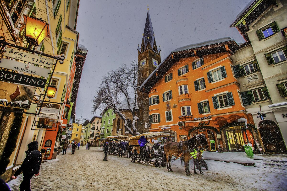 Snowy street in Kitzbühel's old town with a horse-drawn carriage and orange façades