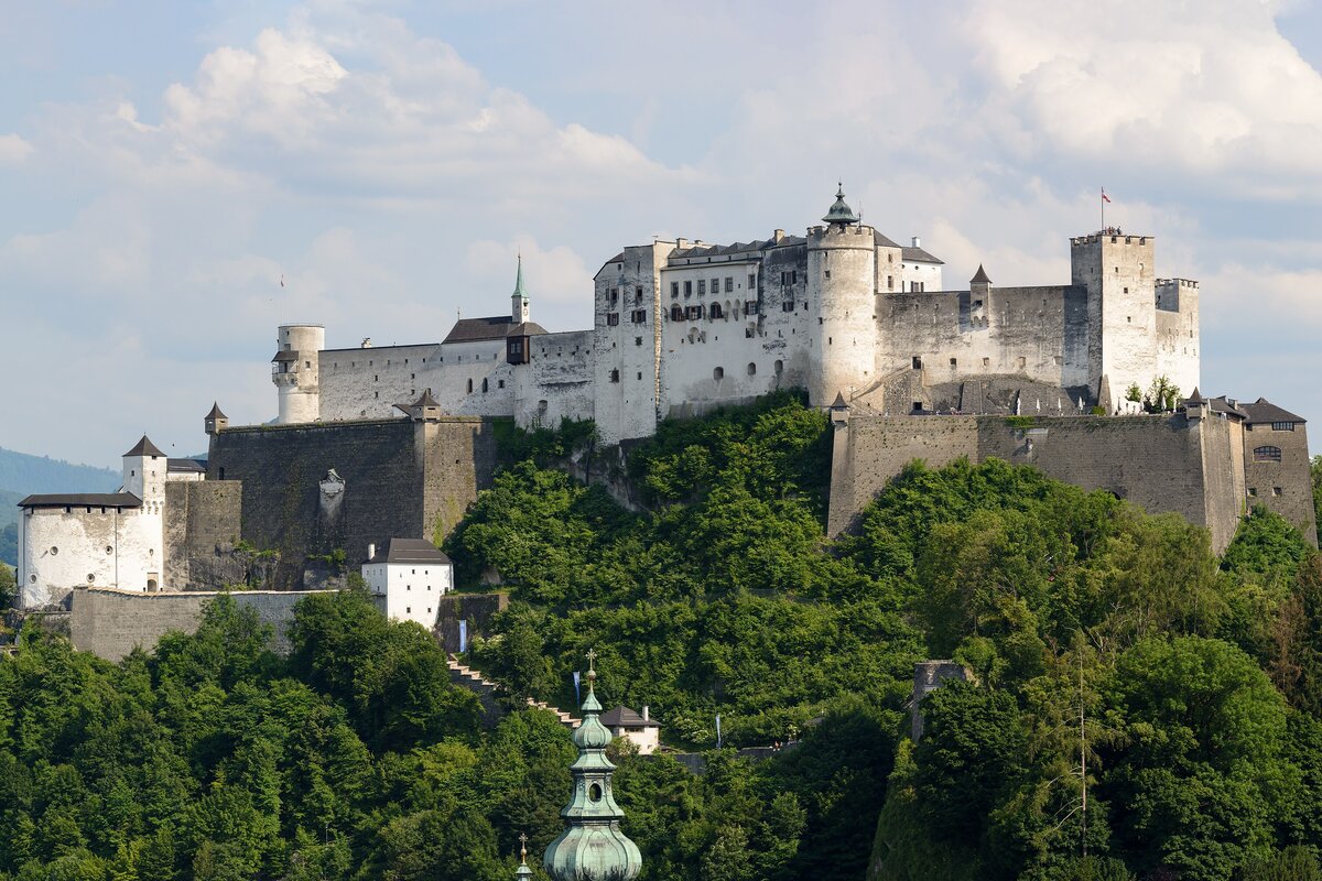 Hohensalzburg Fortress on its wooded hill, with a green church spire in the foreground