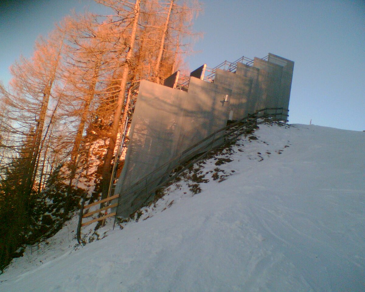 Protective screens beside the Mausefalle section of the Streif, with bare larch trees above a groomed slope