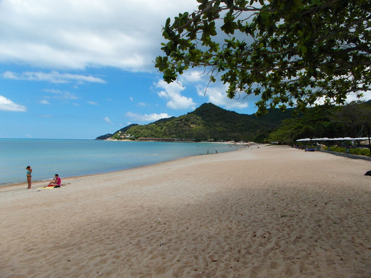 Long sandy beach at Chaweng Noi with hills, palms and boats offshore
