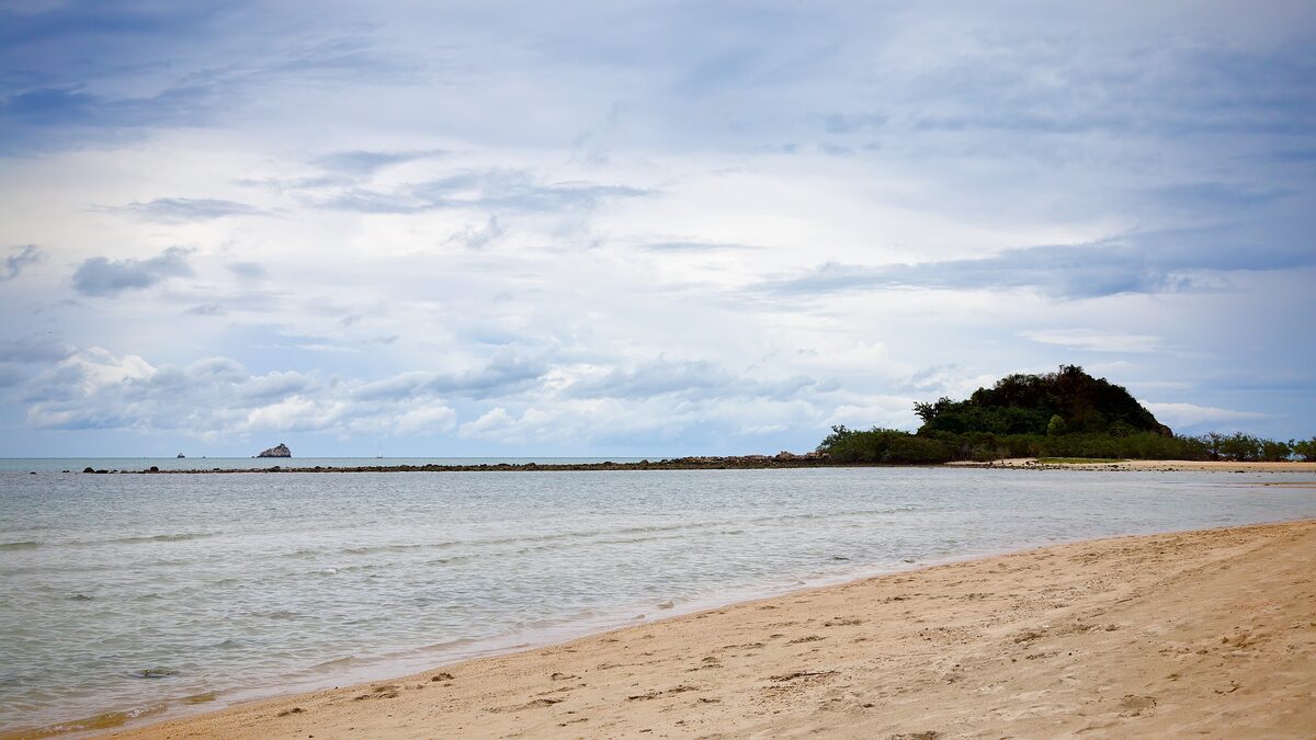 Sand beach at Choeng Mon under a blue sky, with a wooded islet across the bay