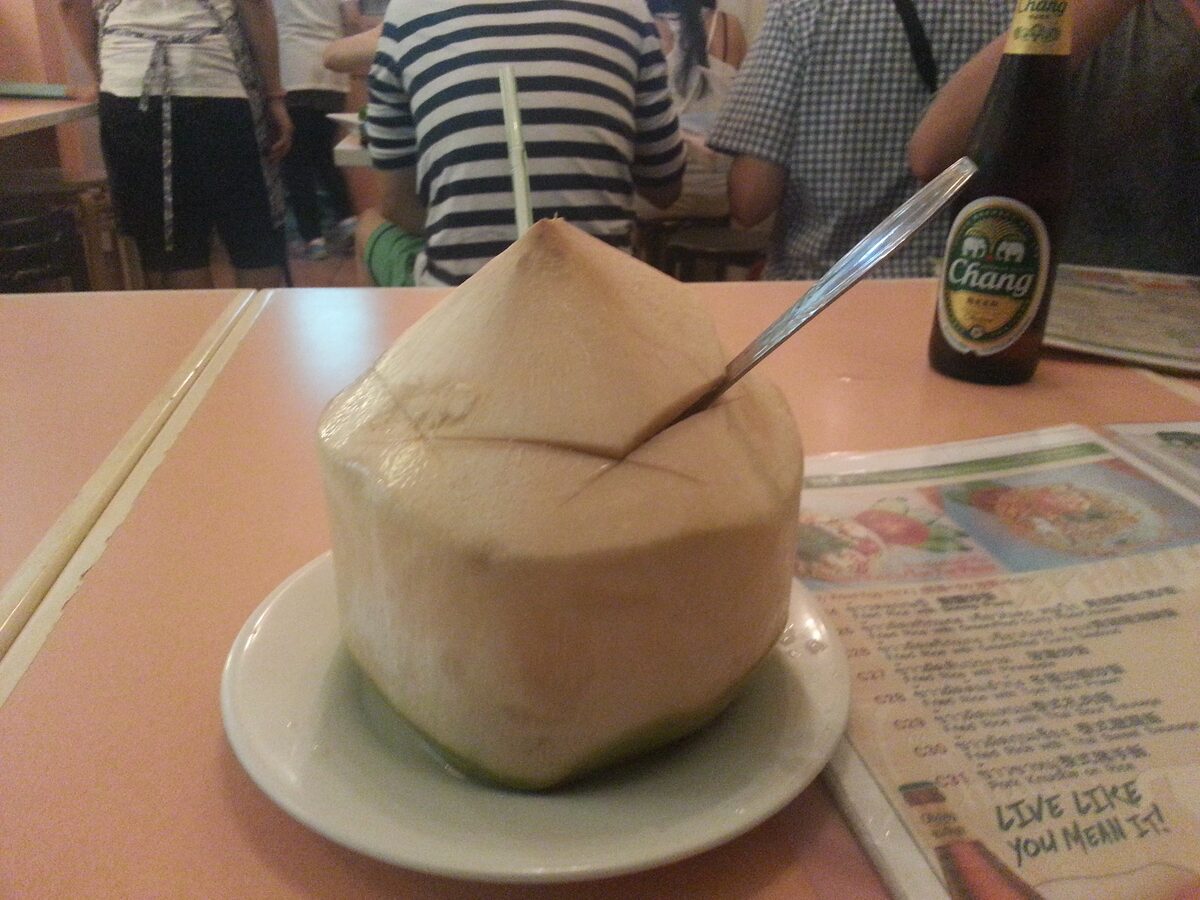 A fresh young coconut with a straw on a plate at a restaurant table