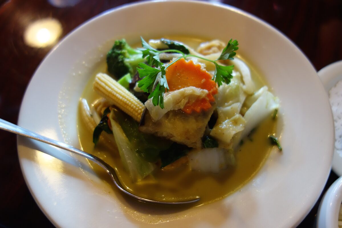 A bowl of green curry with broccoli, baby corn and carrot