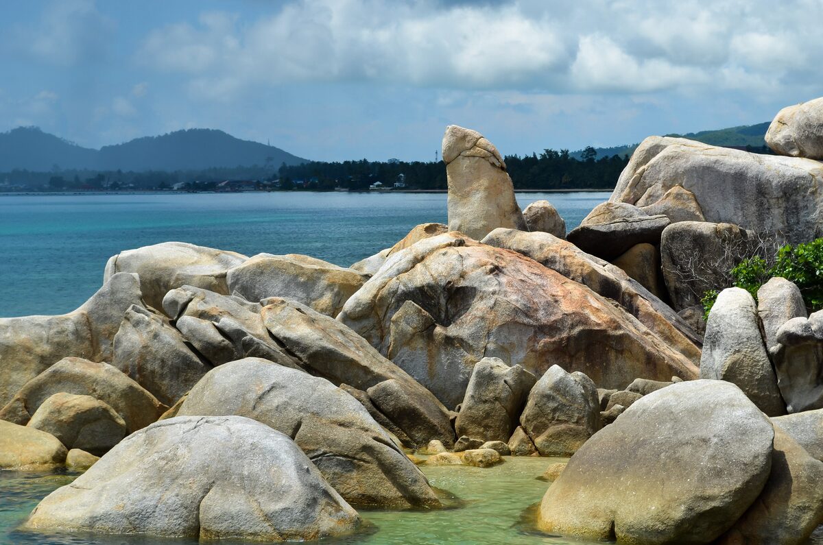 Round granite boulders on the shore at Hin Ta Hin Yai, with the sea and hills behind