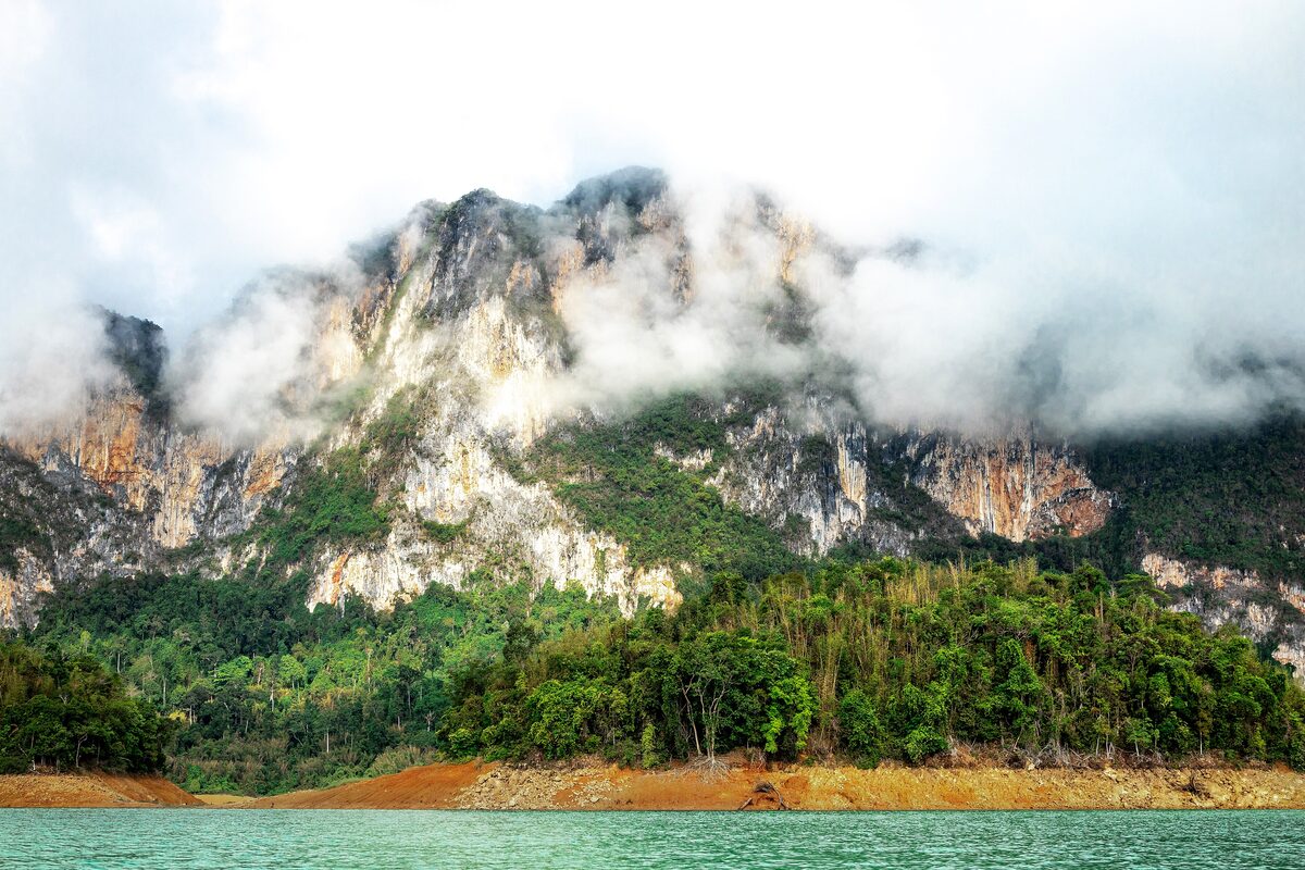 Limestone peaks wrapped in mist above forest and water in Khao Sok National Park