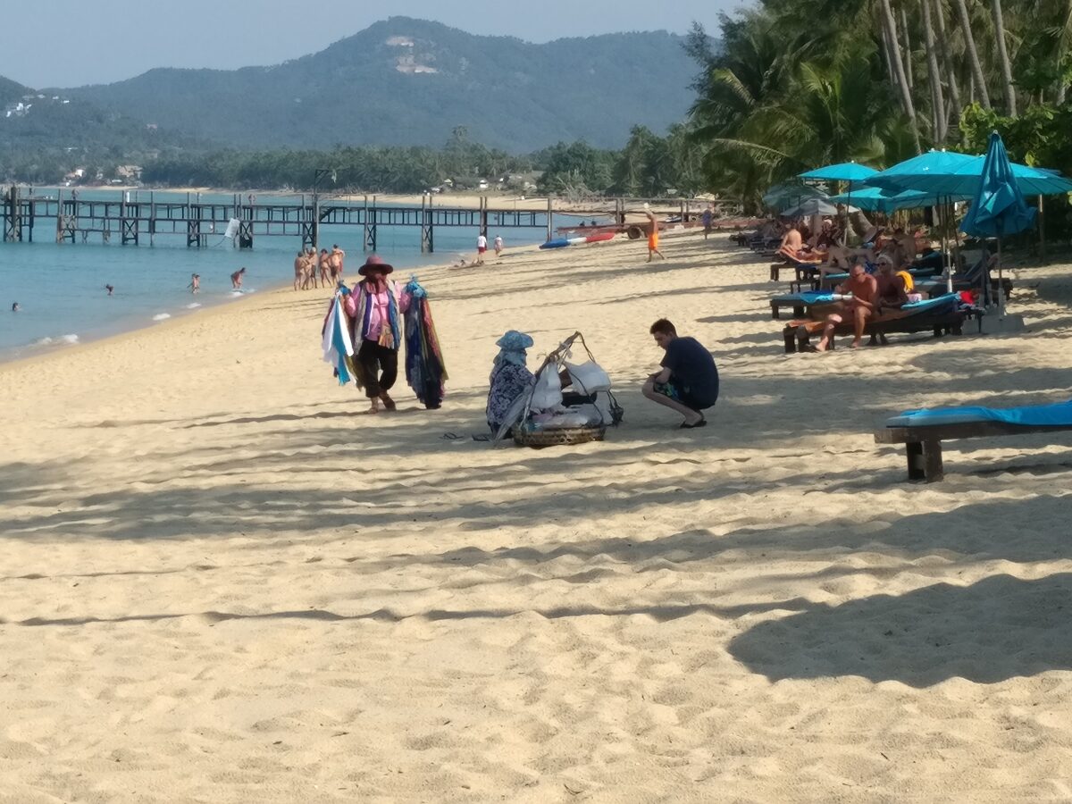 Sand beach at Mae Nam with palms, beach loungers and a long wooden pier