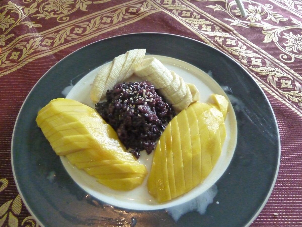 Sliced mango with sticky rice and black sticky rice on a plate with coconut cream