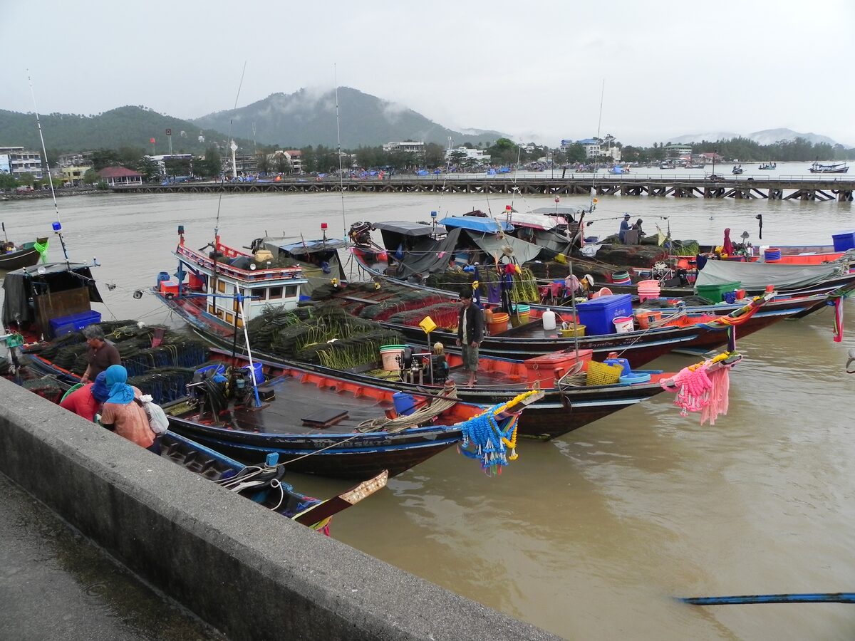 Colorful wooden fishing boats moored beside the pier at Nathon, with the waterfront town and hills behind