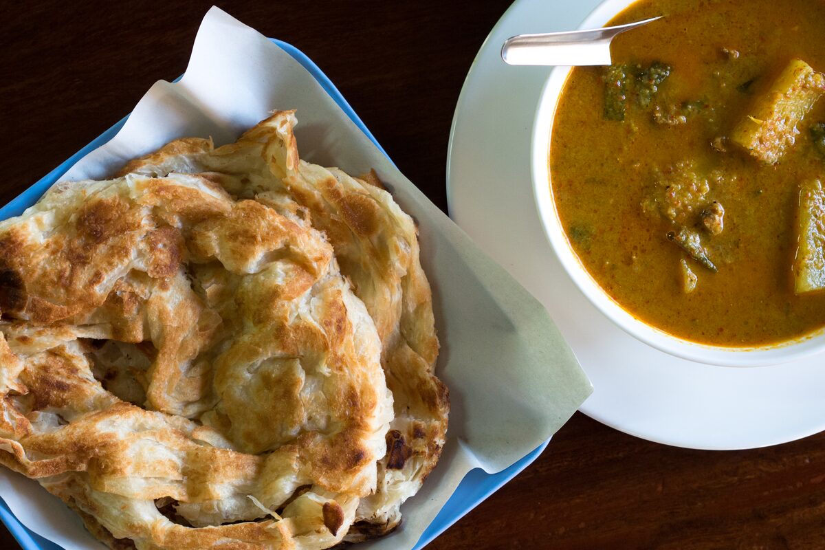 Flaky roti beside a bowl of curry with potato