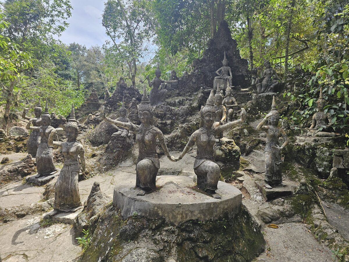 Weathered stone statues among rocks and trees in the Secret Buddha Garden