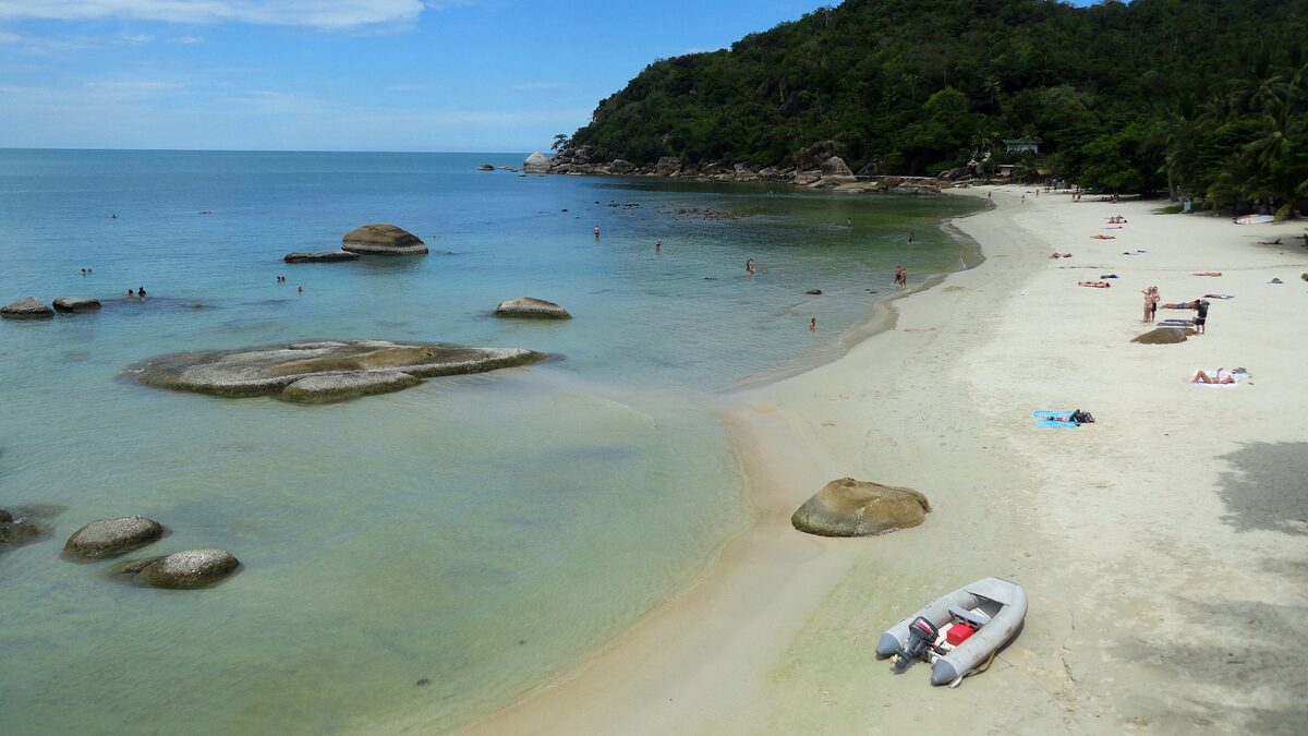 Clear turquoise water, granite rocks and a white sand beach below a forested headland at Silver Beach, with swimmers and sunbathers