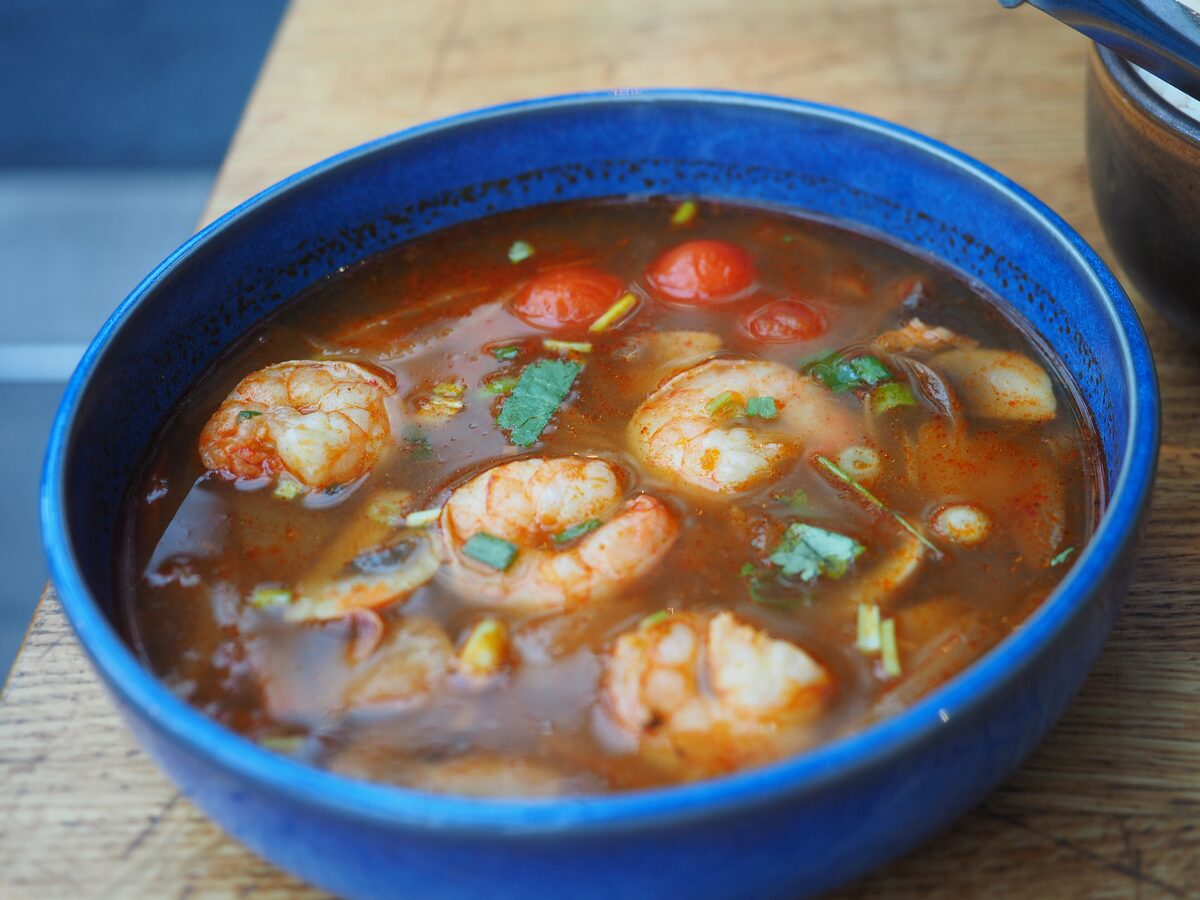 Tom yum soup with shrimp, cherry tomatoes and cilantro in a blue bowl