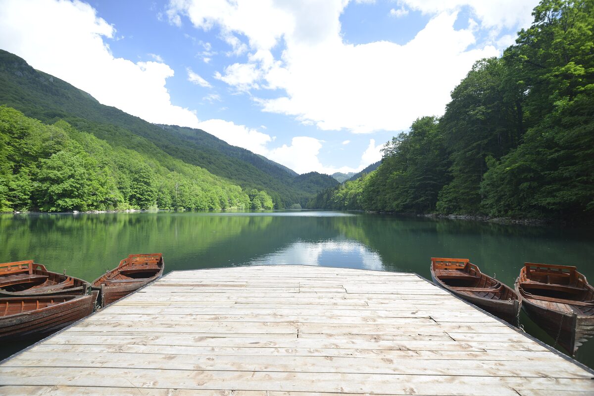 Biogradsko Jezero in late spring: a wooden jetty with rowing boats on still green water, with beech forest on both shores