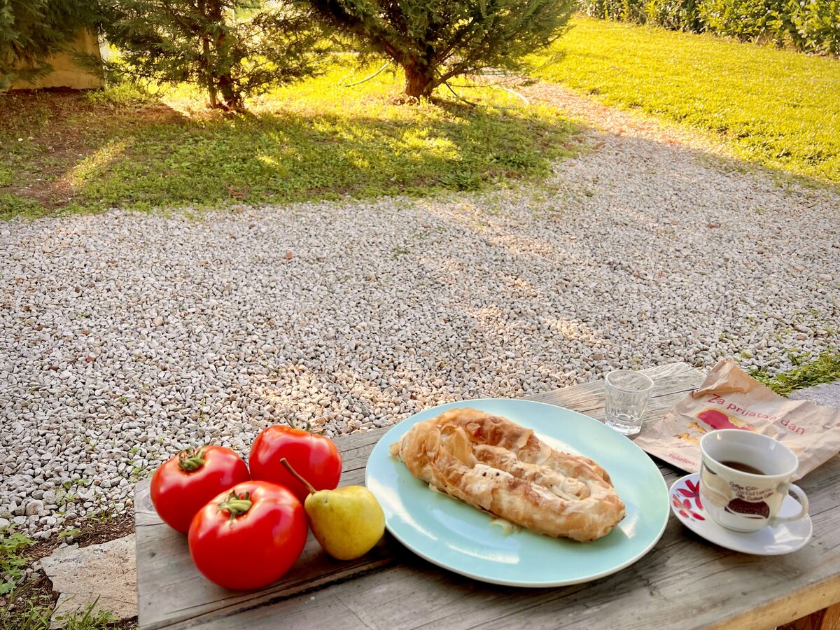 A rolled pie on a plate with tomatoes, a lemon and a small cup of coffee at an outdoor wooden table