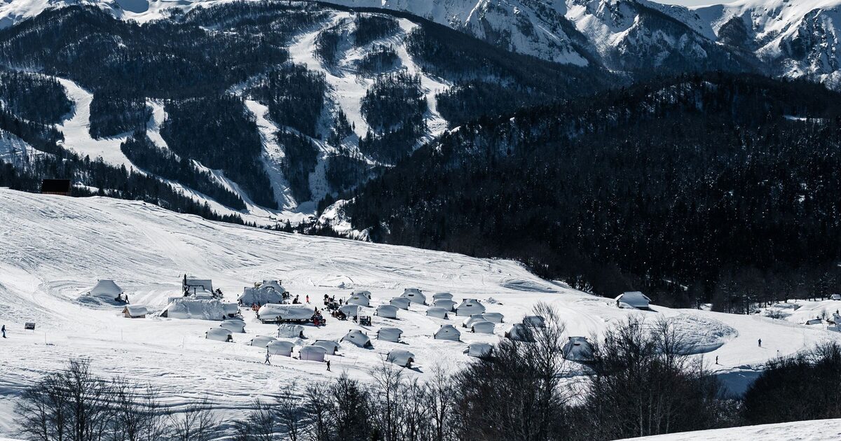 Snow-covered mountains near Kolašin in winter, with ski runs cutting through the dark forest above a hamlet of huts on a white hillside